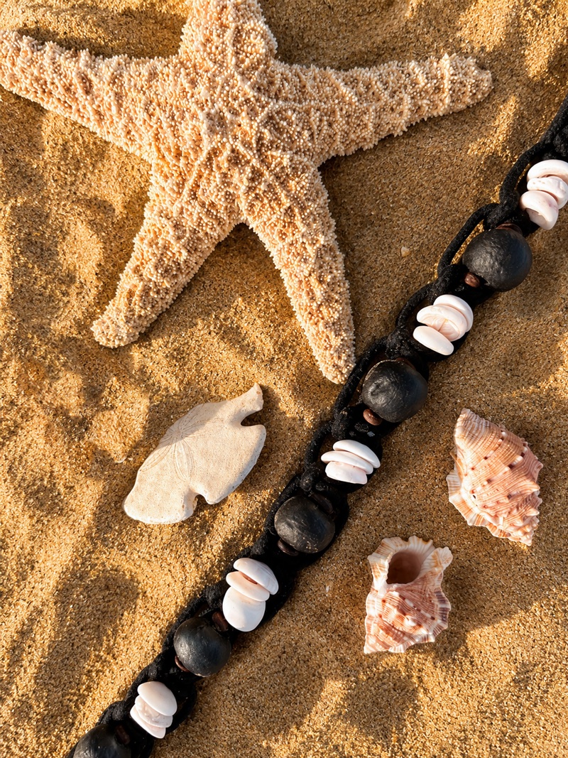 Lava Black Sea Glass & Puka Shell collar, Sand, flat lay on the beach