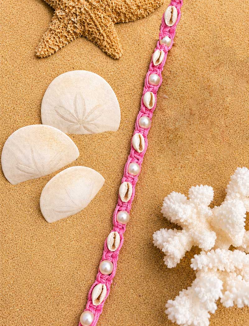 Cowrie & Pearl collar flat lay with shells and starfish on the sand